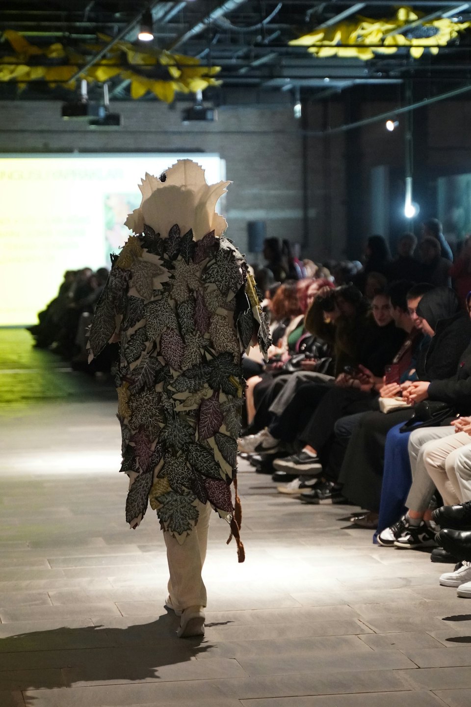 Model walks the runway wearing a textured leafy garment.