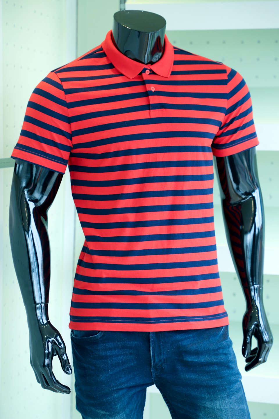 Black mannequin wearing a striped polo shirt and denim jeans.