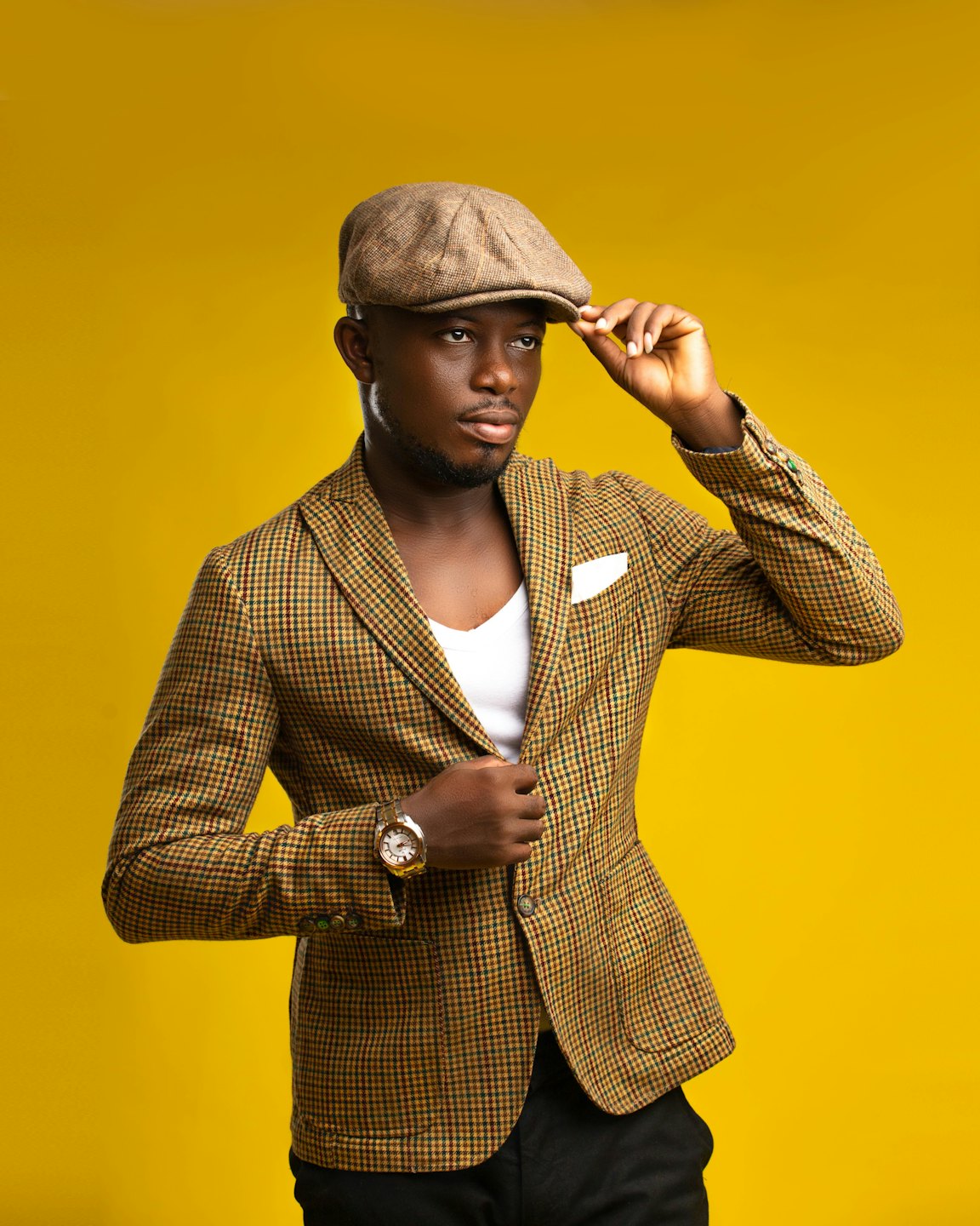 Man in a checkered blazer and flat cap adjusts his jacket.