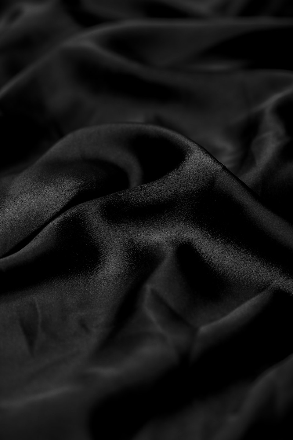 Black satin fabric draped in smooth ripples and folds.