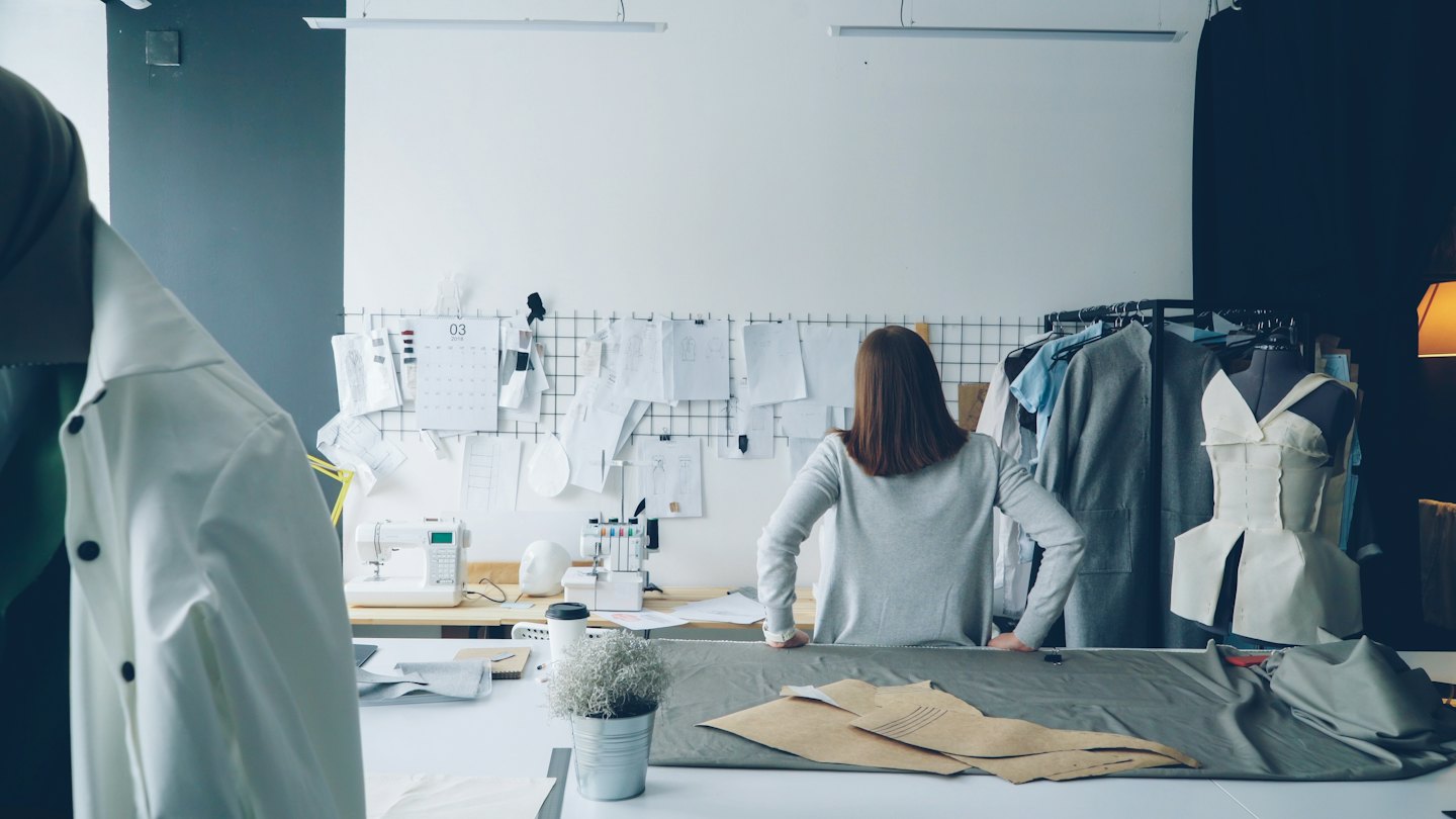Fashion designer reviews fabric patterns at a studio workstation.